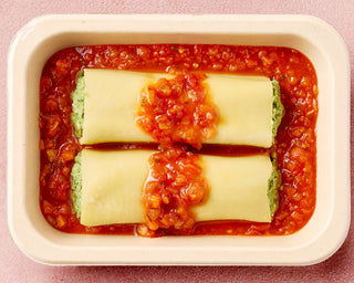 Lasagna rolls in a red sauce in a white dish on a pink background