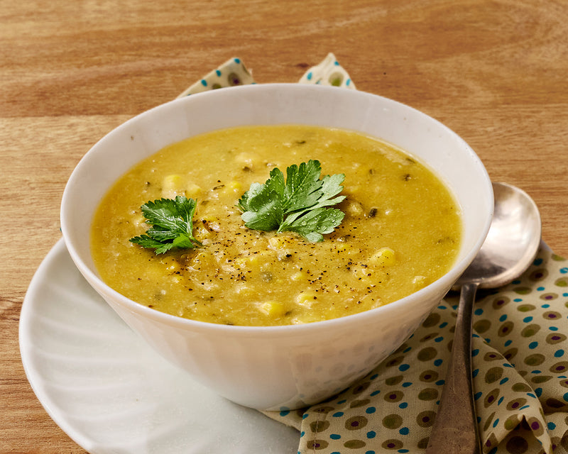 Bowl of Chicken and Corn soup with green garnish on a wooden table