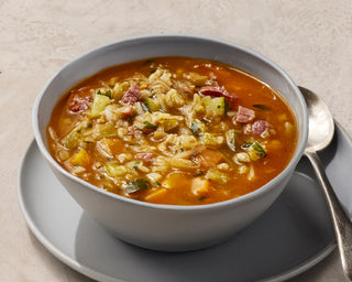 Bowl of soup with vegetables and a spoon on a beige background