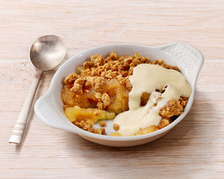 Bowl of dessert with crumble topping and vanilla sauce on a wooden surface