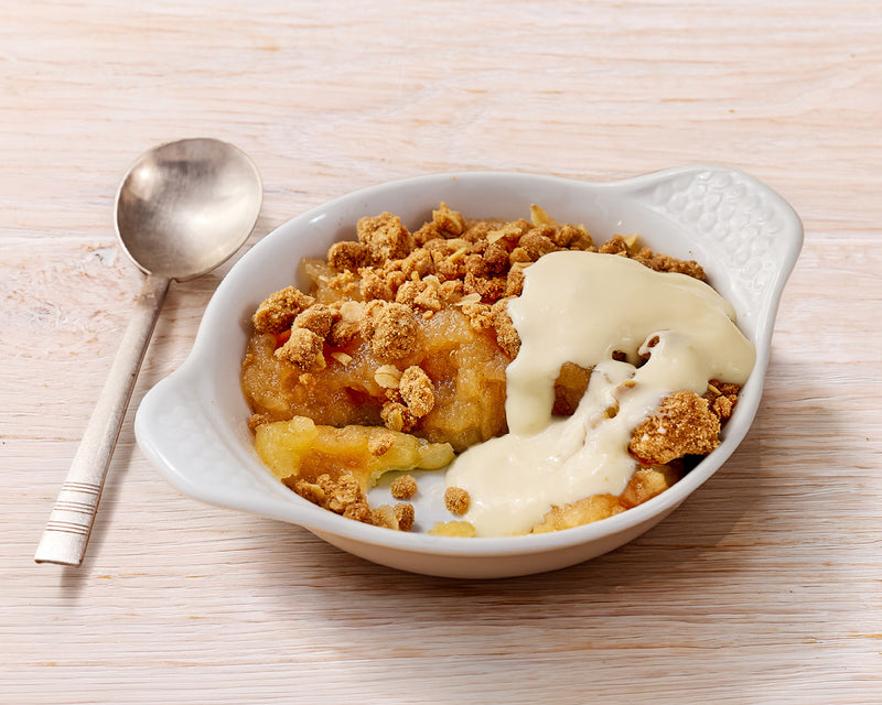 Bowl of dessert with crumble topping and vanilla sauce on a wooden surface