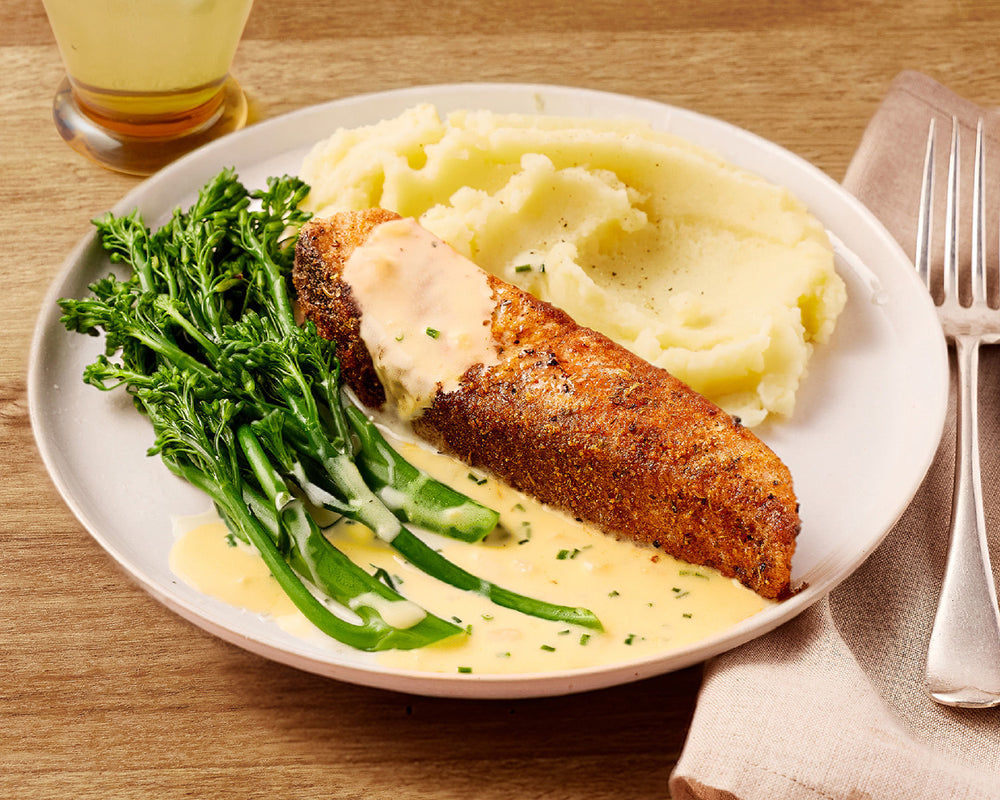 Plated meal with baked salmon, mashed potatoes, and greens on a wooden table.