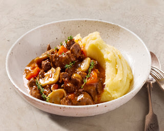 Bowl of beef stew with mashed potatoes on a beige background