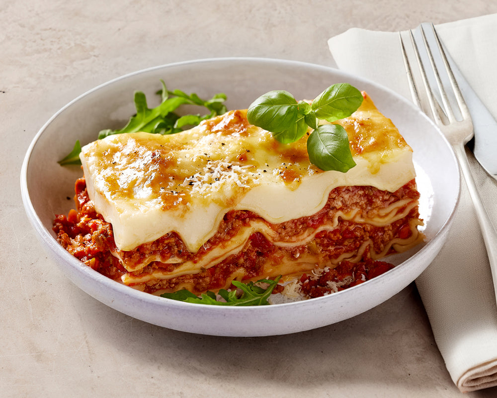 Bowl of lasagna with greens on a beige background
