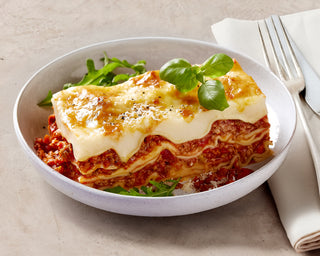 Bowl of lasagna with greens on a beige background