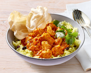 Bowl of butter chicken curry with rice on a wooden table.