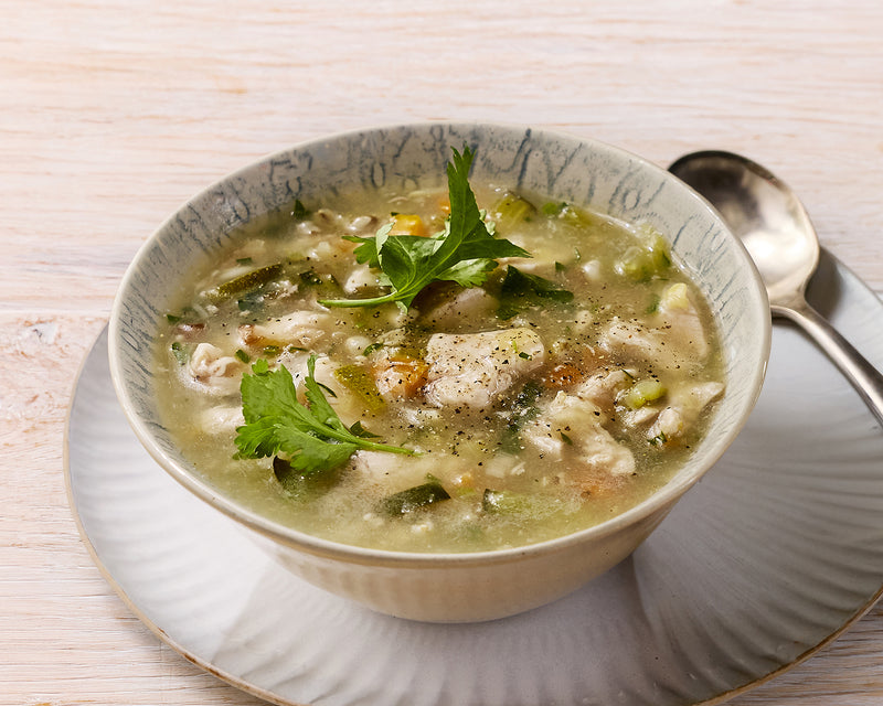 Bowl of soup with greens and a spoon on a wooden table
