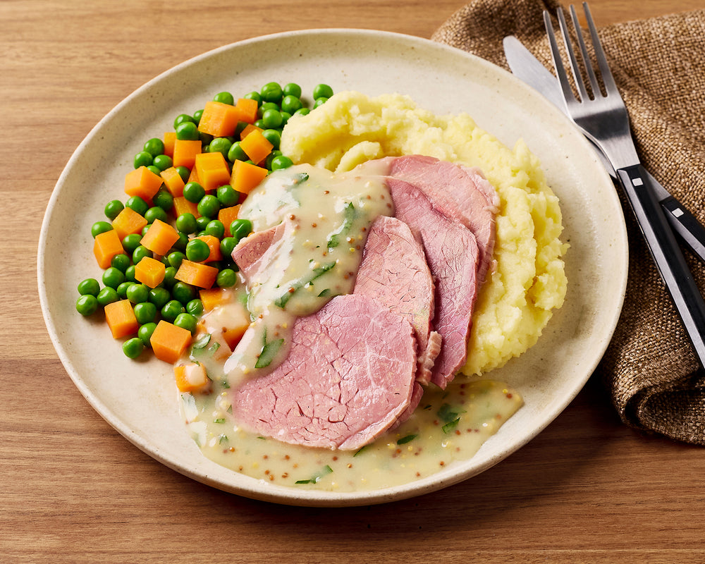 Plate of food with corned beef, mashed potatoes, and vegetables on a wooden table.