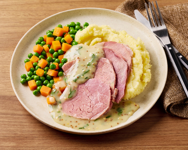 Plate of food with corned beef, mashed potatoes, and vegetables on a wooden table.