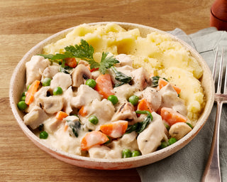 Bowl of chicken and vegetable stew with mashed potatoes on a wooden table.