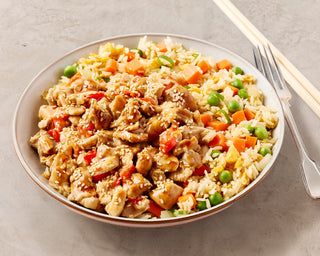 Plated dish of fried rice with vegetables and honey lemon chicken on a gray surface with chopsticks and a fork.