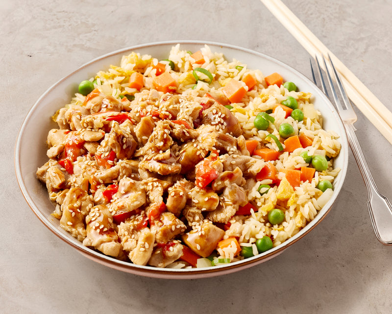 Plated dish of fried rice with vegetables and honey lemon chicken on a gray surface with chopsticks and a fork.