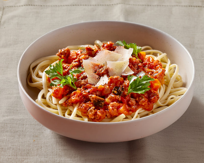 Bowl of spaghetti with tomato sauce, cheese, and parsley on a beige background