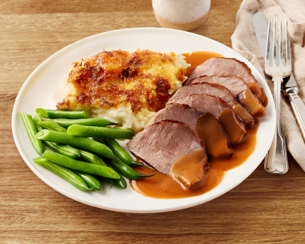 Plated meal with sliced roast beef, green beans, and mashed potatoes on a wooden table.