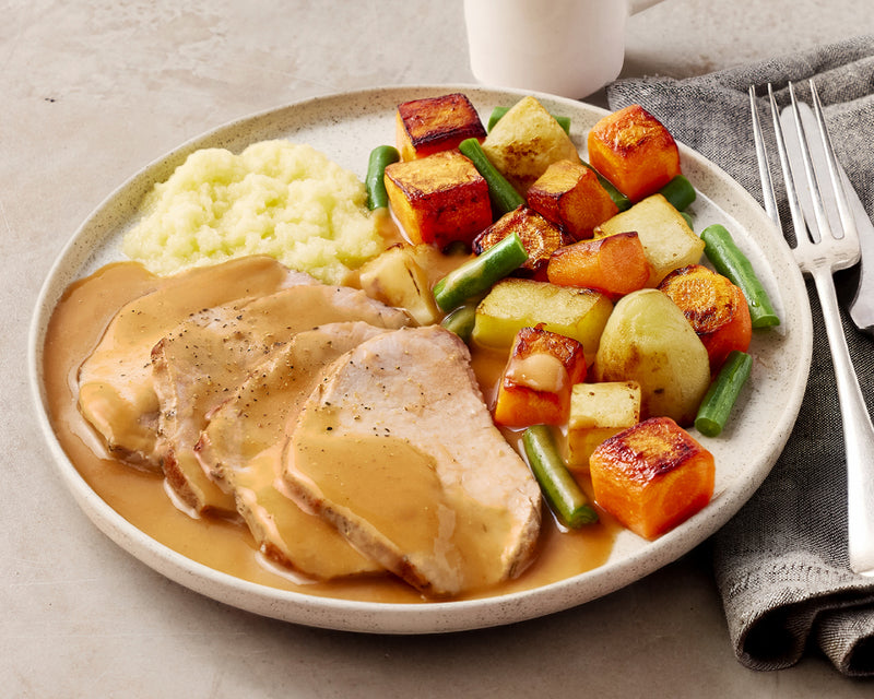 Plated meal with sliced pork roast, vegetables, and mashed potatoes on a beige plate.