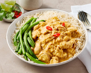 Bowl of satay chicken with rice and green beans on a beige surface