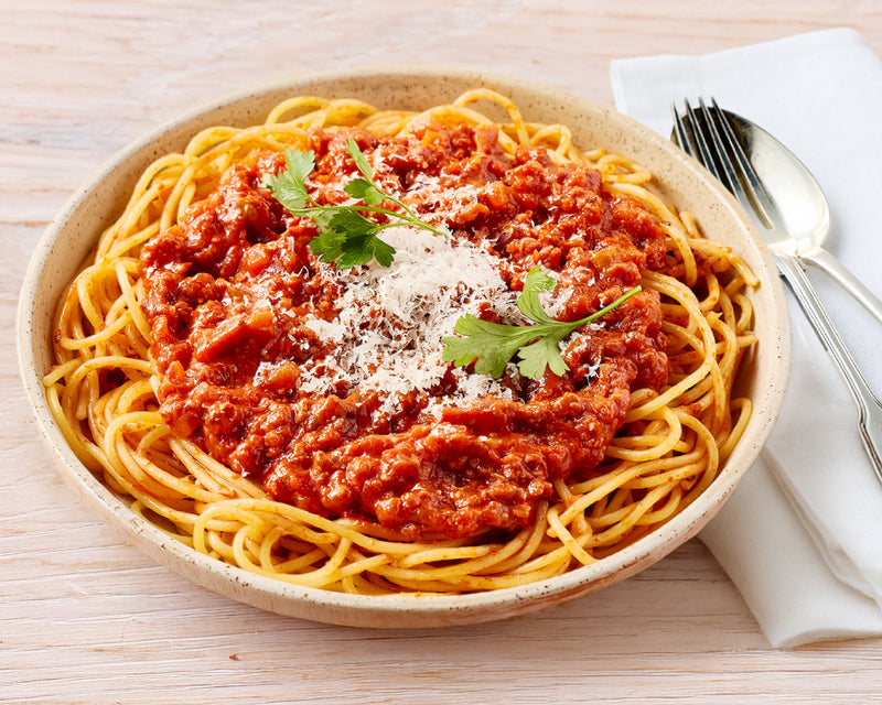 Spaghetti dish with bolognese sauce, parmesan cheese, and parsley in a beige bowl on a wooden table.