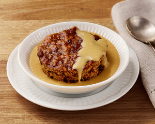 Sticky Date pudding with butterscotch custard in a white bowl on a wooden table.