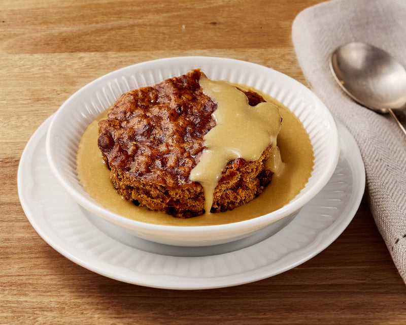 Sticky Date pudding with butterscotch custard in a white bowl on a wooden table.