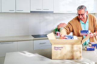 Man in a kitchen opening a box labeled 'Dineamic HeyDuy' and looking at meals.