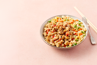 Bowl of fried rice with vegetables on a pink background