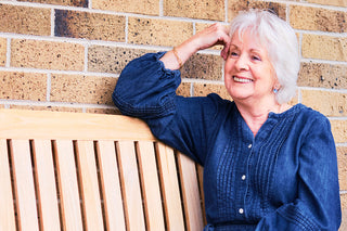 Woman in a blue shirt sitting on a wooden bench against a brick wall