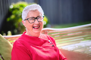 Woman with glasses wearing a red sweater, sitting outdoors.