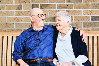 A couple sitting on a bench with a brick wall background