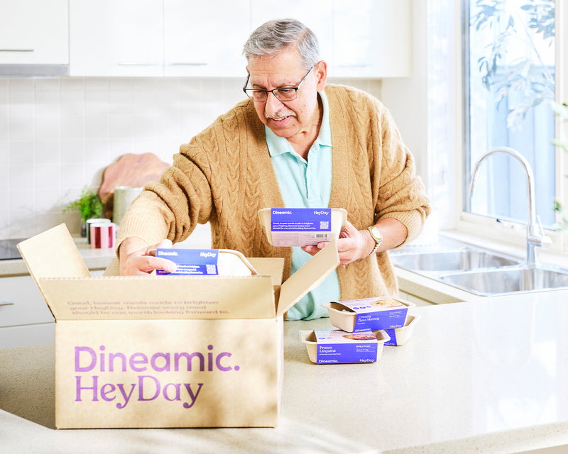 Man unpacking a box labeled 'Dineamic HeyDay' in a kitchen.